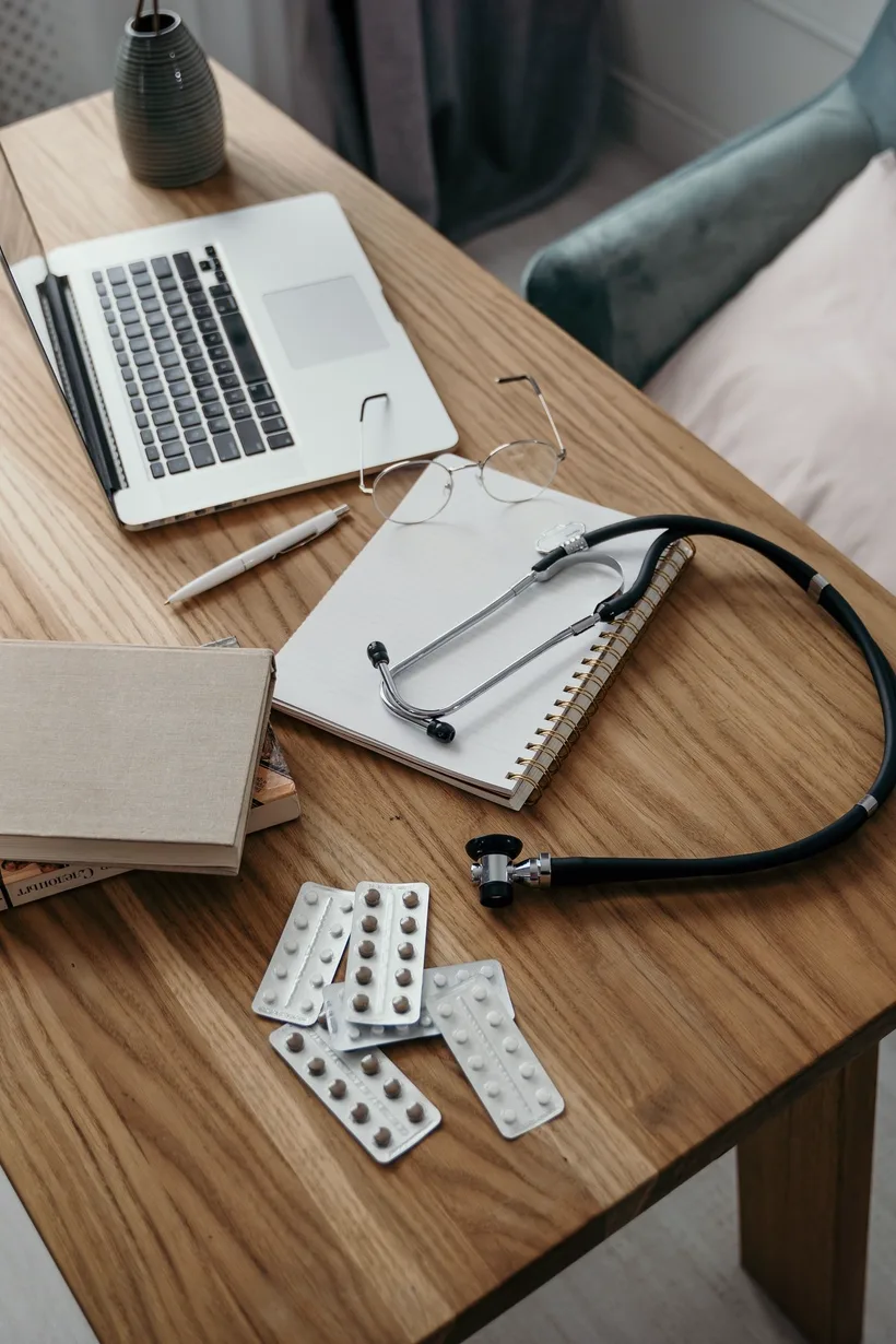 Laptop, estetoscópio e cartelas de remédio na mesa