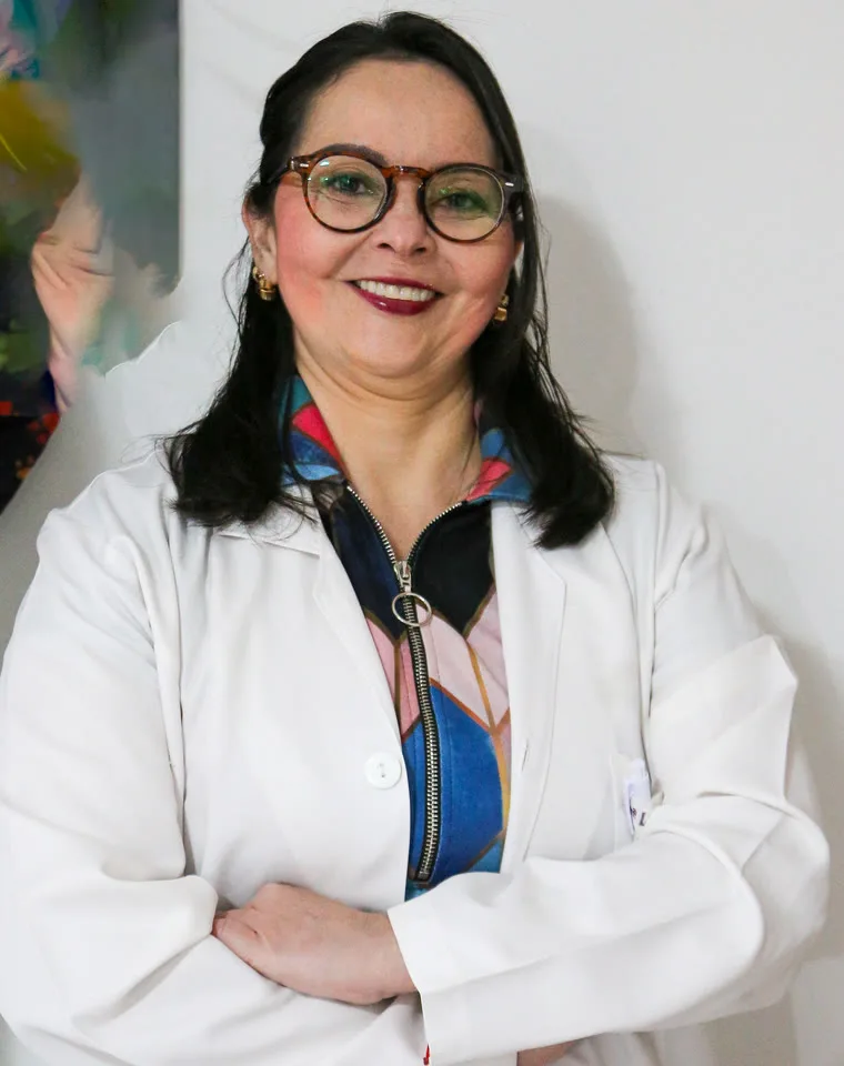 Dra. Larissa Jardim Amorim, de jaleco branco e braços cruzados, em pé na clínica